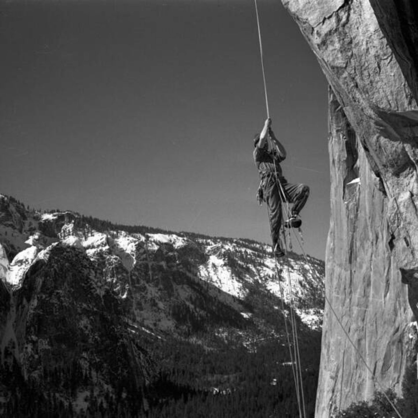 Black and white photo print featuring a person climbing a rock face with a mountain in the background.