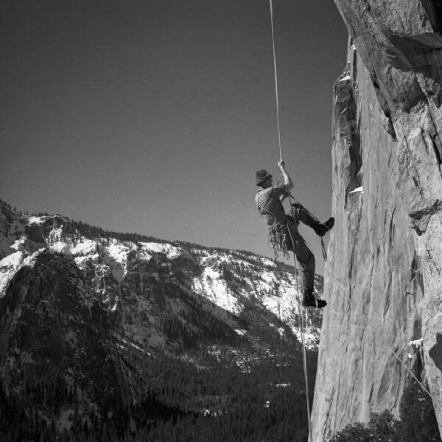 Black and white photo print of a person climbing a rock wall with a scenic view of mountains in the background.