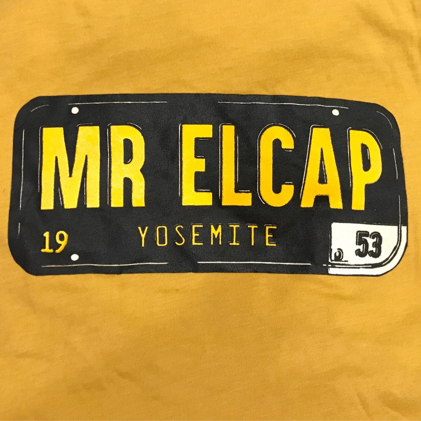 A yellow t-shirt with a graphic print of a license plate that says 'MR ELCAP' and 'Yosemite' on it.