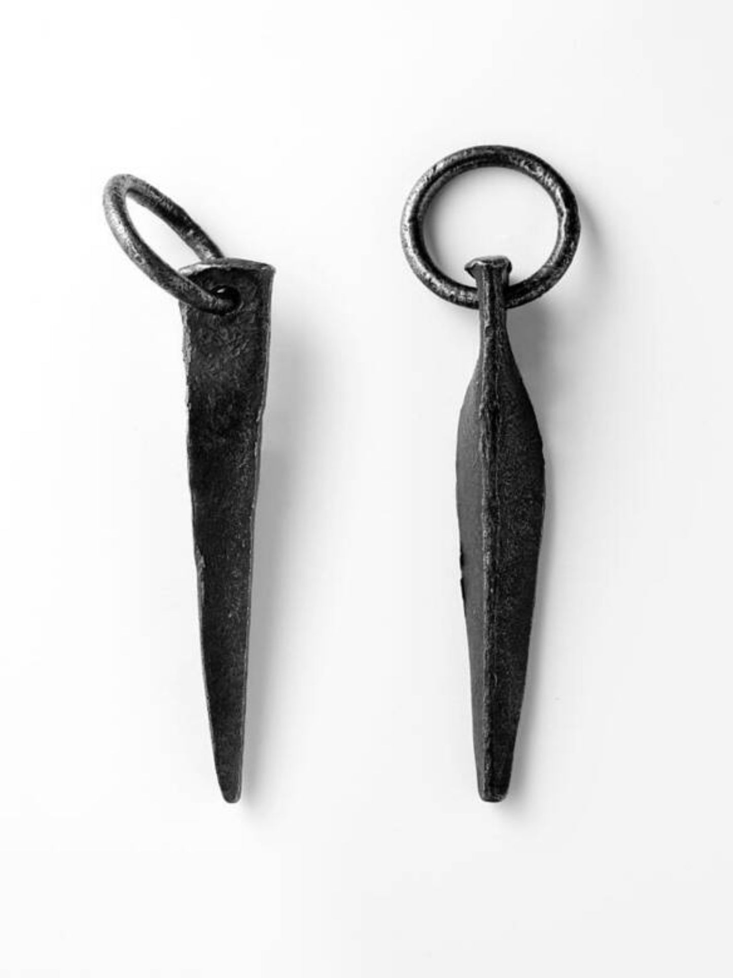 Two black metal pitons with a ring attached at the top, displayed against a white background.